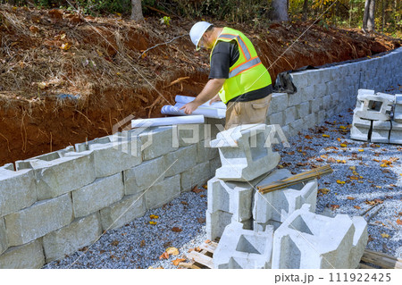 Construction workers typically use blueprints when mounting cement blocks as retaining walls 111922425
