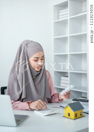 muslim woman with hijab using calculator focus on utility bills calculate check credit card receipt monthly expense 111923056