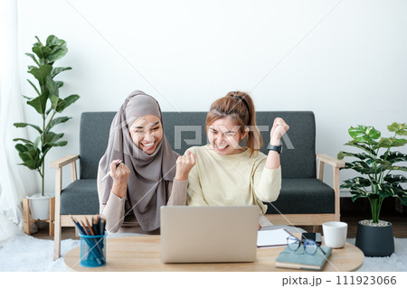 Happy beautiful diverse Asian women working and discussing together in the pantry area in co-working space, female students using laptop - notebook computer. Asian women colleague having a discussion. 111923066