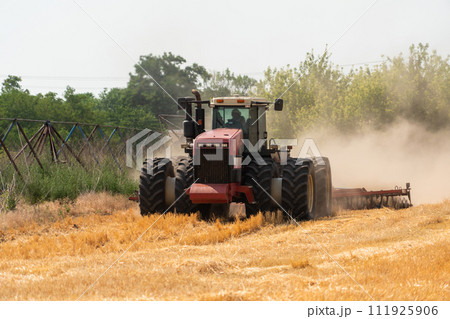 A tractor with a plow plows the field after harvesting. A tractor with a plow plows the field after harvesting. 111925906