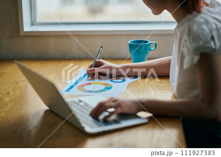 パソコンをタイピングしながら書類にメモをする若い女性 111927385