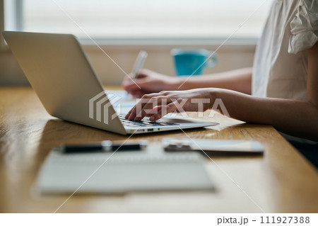 パソコンをタイピングしながらメモをする若い女性 111927388