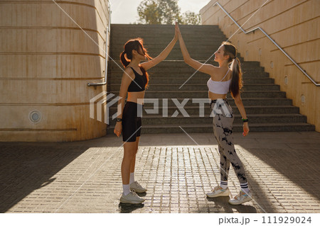 Happy female friends doing gesture of sport shake hand after exercising outside 111929024