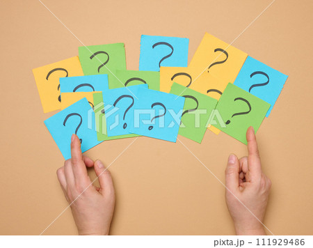 Female hands hold paper sheets with a drawn question mark on a beige background Female hands hold paper sheets with a drawn question mark on a beige background 111929486