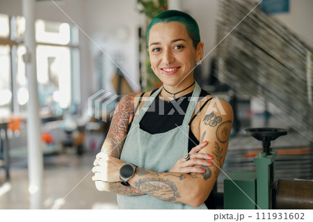Smiling female designer standing with crossed hands on background of workshop and looks camera 111931602