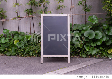 Blank white outdoor advertising stand/sandwich board mock up template. Clear street signage board placed by an outdoor dinning area of a restaurant. Background texture of standee on street. Blank white outdoor advertising stand/sandwich board mock up template. Clear street signage board placed by an outdoor dinning area of a restaurant. Background texture of standee on street. 111936210