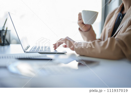 Businesswomen drinking coffee and working to analysis strategy and management about new startup project while typing report about investment and financial of business on digital laptop in workplace 111937019