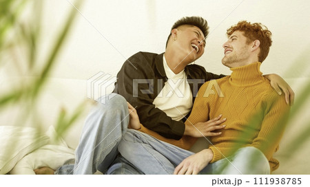 Gay couple laughing while sitting on the sofa 111938785