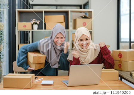 Friend muslim female two work business sme online shopping working on laptop computer with parcel box on desk at home, SME online business and delivery concept 111940206
