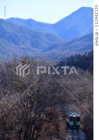 冬枯れの針葉樹の森を抜けてやってきた小海線ローカル列車 111942131