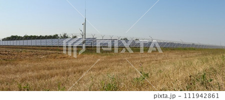 a dry field with solar panels surrounded by a fence on a sunny day as an example of the work of environmentally friendly technologies, a country landscape with batteries of a modern power plant a dry field with solar panels surrounded by a fence on a sunny day as an example of the work of environmentally friendly technologies, a country landscape with batteries of a modern power plant 111942861