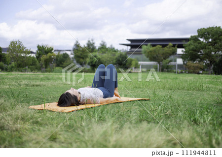 ヨガウェアを着て公園で仰向けになる女性 ヨガウェアを着て公園で仰向けになる女性 111944811