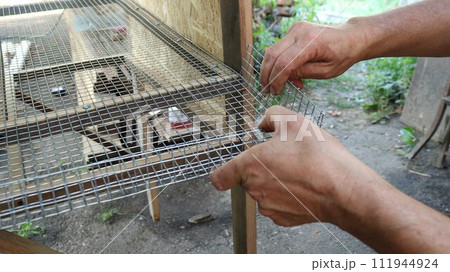 male hands bend the mesh side of the metal lattice base of a cage for domestic quails in the production process, forming a rise in the edge of the cage base for small farm poultry 111944924