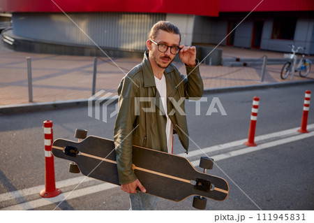Portrait of handsome casual guy with skateboard over downtown background 111945831