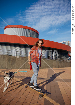 Hipster guy riding skateboard with dog on leash enjoying summer time Hipster guy riding skateboard with dog on leash enjoying summer time 111945943