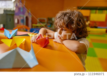 Cute boy child playing handmade origami paper boat at childcare center 111946071