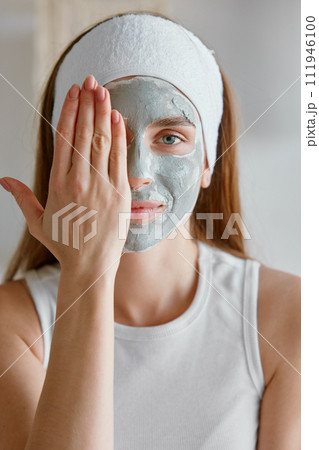 Portrait of young woman with clay facial cosmetology mask Portrait of young woman with clay facial cosmetology mask 111946100