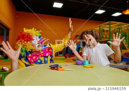 Funny clown and boy fooling around while drinking tea from toy cup 111946159