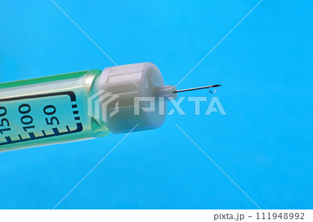 A drop of medicine at the end of a syringe needle with dosage divisions close-up on a blue background. Vaccination of the population 111948992