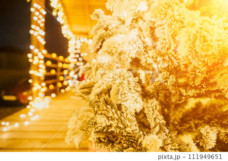Snow-covered Christmas tree with bright white lights situated outdoors near a building, a welcoming festive moment. Snow-covered Christmas tree with bright white lights situated outdoors near a building, a welcoming festive moment. 111949651