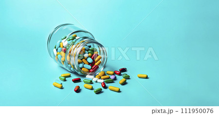 Multi-colored pills in a jar lie scattered on the table on a light blue background 111950076
