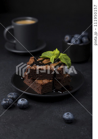 Chocolate brownie cake with mint, blueberries, chocolate topping and espresso. Traditional American dessert. Popular cake with dark chocolate on a black background. Close-up, selective focus. 111950157