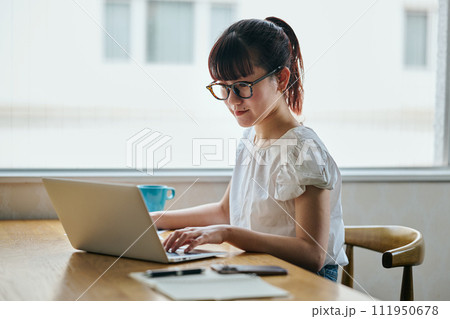 パソコンをタイピングしながら書類にメモをする若い女性 パソコンをタイピングしながら書類にメモをする若い女性 111950678