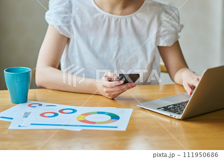 パソコンをタイピングしながらスマホを操作する若い女性 111950686