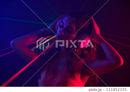 Woman in headphones dancing in neon lights in night club Woman in headphones dancing in neon lights in night club 111952155