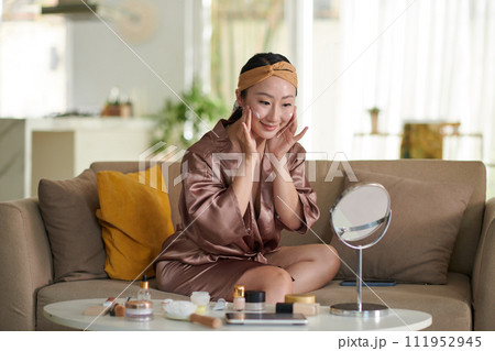 Smiling young woman applying brightening face mask after cleaning face Smiling young woman applying brightening face mask after cleaning face 111952945