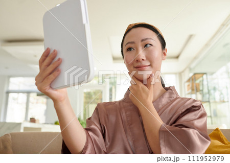 Smiling young woman looking at mirror after applying natural makeup 111952979