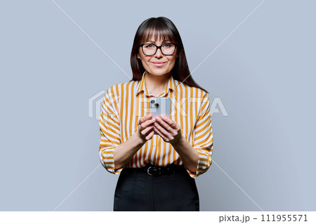 Middle aged smiling woman with smartphone on grey studio background 111955571