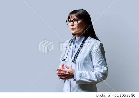 Smiling mature woman doctor, profile view, gray background, copy space 111955580