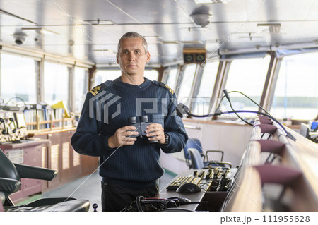 Deck officer with binoculars on navigational bridge. Seaman on board of vessel. Commercial shipping. Cargo ship. Deck officer with binoculars on navigational bridge. Seaman on board of vessel. Commercial shipping. Cargo ship. 111955628