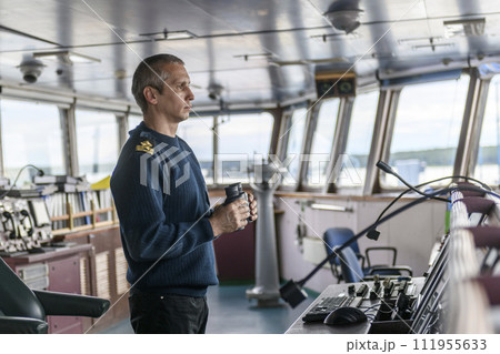 Deck officer with binoculars on navigational bridge. Seaman on board of vessel. Commercial shipping. Cargo ship. Deck officer with binoculars on navigational bridge. Seaman on board of vessel. Commercial shipping. Cargo ship. 111955633