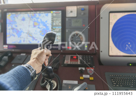Navigational control panel and VHF radio with hand. Radio communication at sea. Working on the ship's bridge. Navigational control panel and VHF radio with hand. Radio communication at sea. Working on the ship's bridge. 111955643