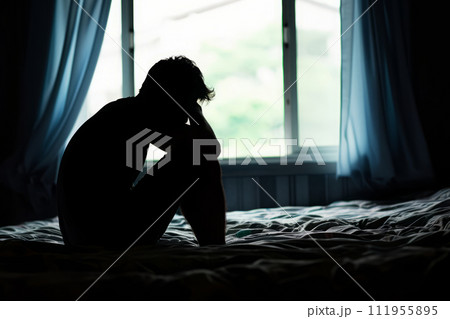Silhouette of depressed man sitting on bed in front of window 111955895
