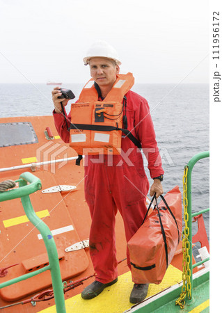 Seaman wearing lifejacket with vhf radio on Muster station. Abandon ship drill. Free fall boat. Cargo vessel. Seaman wearing lifejacket with vhf radio on Muster station. Abandon ship drill. Free fall boat. Cargo vessel. 111956172