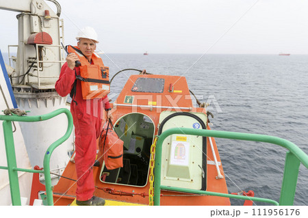 Seaman wearing lifejacket with vhf radio on Muster station. Abandon ship drill. Free fall boat. Cargo vessel. Seaman wearing lifejacket with vhf radio on Muster station. Abandon ship drill. Free fall boat. Cargo vessel. 111956176