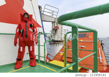 Seaman wearing Immersion Suit on Muster station. Abandon ship drill. Free fall boat. Cargo vessel. Seaman wearing Immersion Suit on Muster station. Abandon ship drill. Free fall boat. Cargo vessel. 111956181