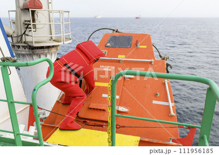 Seaman wearing Immersion Suit on Muster station. Abandon ship drill. Free fall boat. Cargo vessel. 111956185