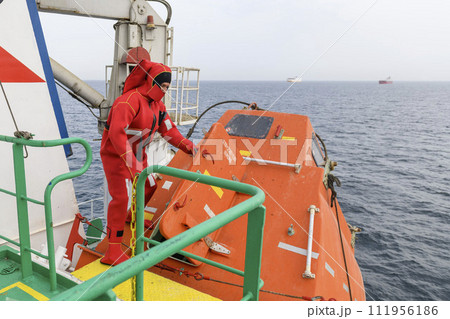 Seaman wearing Immersion Suit on Muster station. Abandon ship drill. Free fall boat. Cargo vessel. Seaman wearing Immersion Suit on Muster station. Abandon ship drill. Free fall boat. Cargo vessel. 111956186