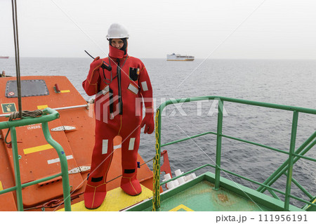 Seaman wearing Immersion Suit on Muster station. Abandon ship drill. Free fall boat. Cargo vessel. Seaman wearing Immersion Suit on Muster station. Abandon ship drill. Free fall boat. Cargo vessel. 111956191