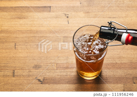 Pouring beer into pint glass on a wooden table Pouring beer into pint glass on a wooden table 111956246