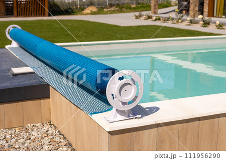 Swimming pool cover for protection against dirt, leaves, heating and cooling water, copy space. Blue tarpaulin pool cover. Summer day Swimming pool cover for protection against dirt, leaves, heating and cooling water, copy space. Blue tarpaulin pool cover. Summer day 111956290
