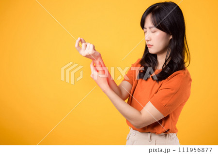 Woman wrist pain due to arthritis showcased in yellow studio portrait. Concept of injury and physical discomfort. Woman wrist pain due to arthritis showcased in yellow studio portrait. Concept of injury and physical discomfort. 111956877