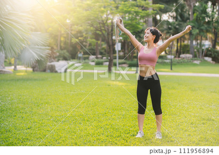 happiness of a fit Asian woman in her 30s, wearing pink sportswear, as she breathes in the fresh air of a public park. Embrace the concept of wellness living and reconnect with nature 111956894