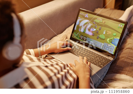 Close up of unrecognizable teenager playing online video games via laptop while lying on bed at night Close up of unrecognizable teenager playing online video games via laptop while lying on bed at night 111958860