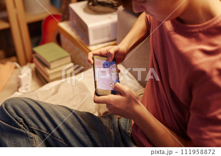 Close up of teenage boy playing online mobile game via smartphone with focus on phone screen 111958872