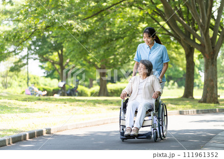 車椅子のシニア女性と介護士の若い女性 車椅子のシニア女性と介護士の若い女性 111961352